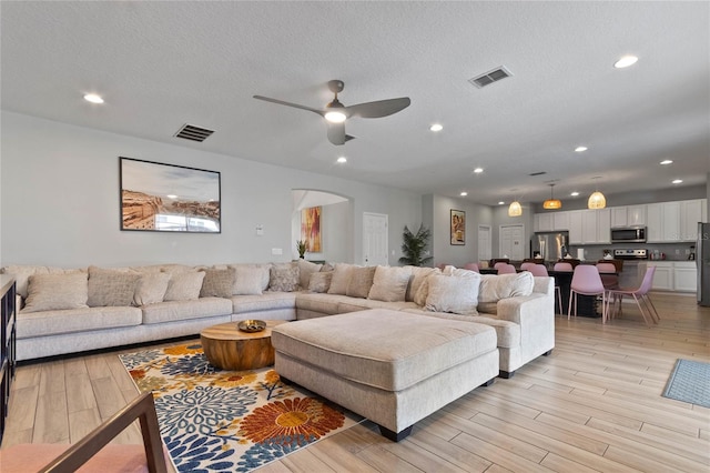 living room featuring ceiling fan, light hardwood / wood-style flooring, and a textured ceiling