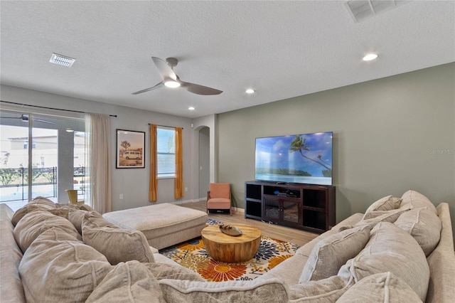 living room with a textured ceiling, ceiling fan, and light wood-type flooring