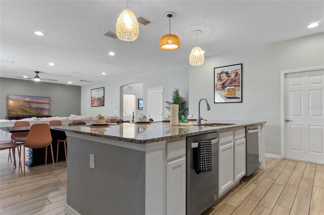 kitchen with an island with sink, pendant lighting, ceiling fan, light hardwood / wood-style flooring, and white cabinetry