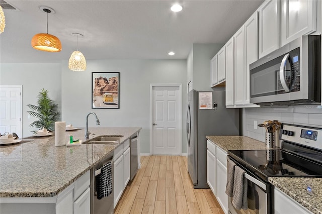 kitchen featuring light hardwood / wood-style flooring, appliances with stainless steel finishes, white cabinets, hanging light fixtures, and sink