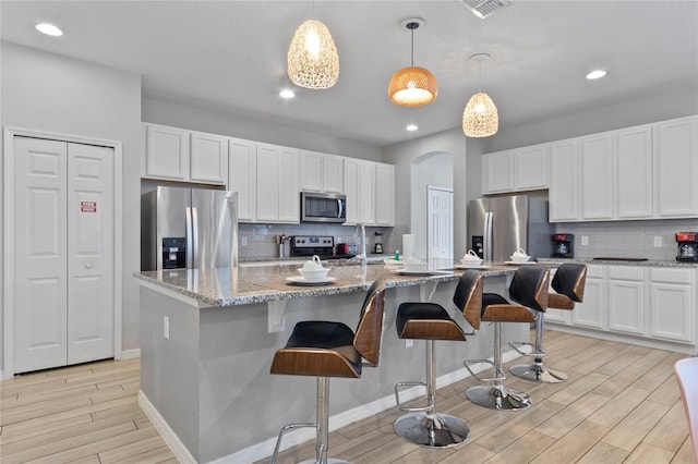 kitchen with backsplash, stainless steel appliances, a kitchen bar, and decorative light fixtures