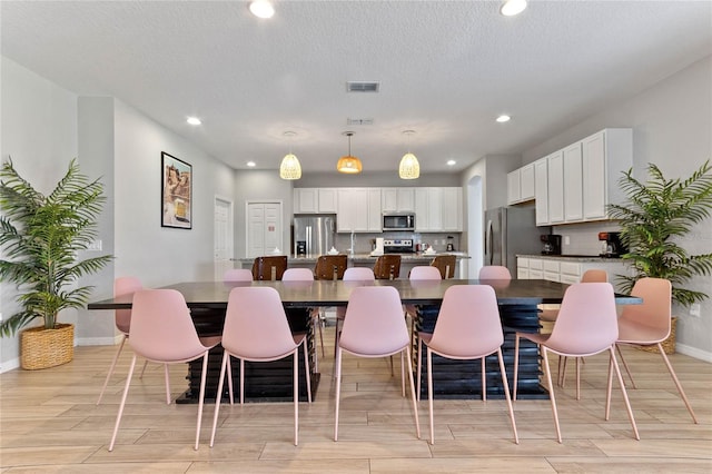 kitchen featuring pendant lighting, white cabinets, stainless steel appliances, a kitchen bar, and a textured ceiling