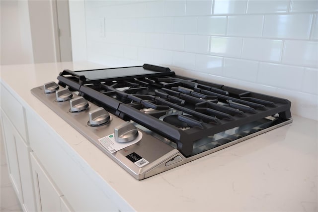 room details featuring white cabinetry, decorative backsplash, and stainless steel gas cooktop