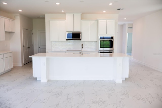 kitchen with sink, appliances with stainless steel finishes, tasteful backsplash, an island with sink, and white cabinets