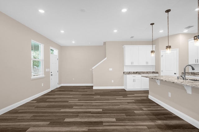 kitchen with dark wood-type flooring, sink, white cabinets, light stone counters, and pendant lighting