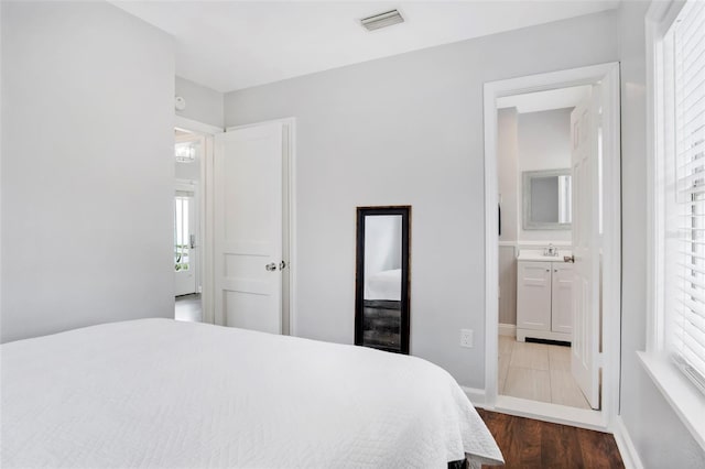 bedroom featuring ensuite bath, hardwood / wood-style floors, sink, and multiple windows