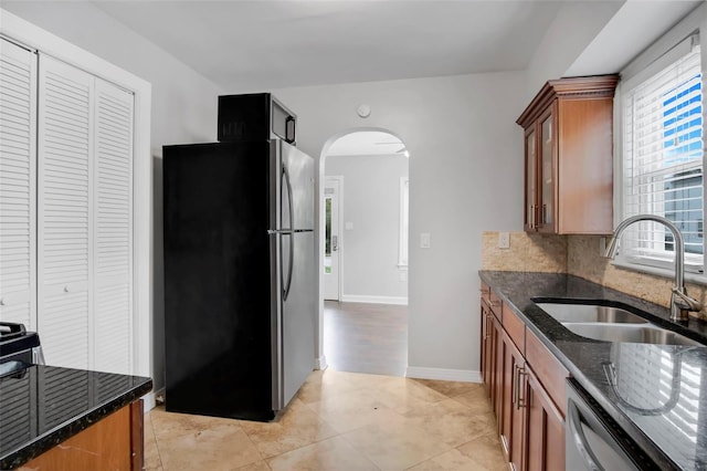 kitchen featuring sink, light tile floors, dark stone countertops, backsplash, and stainless steel appliances