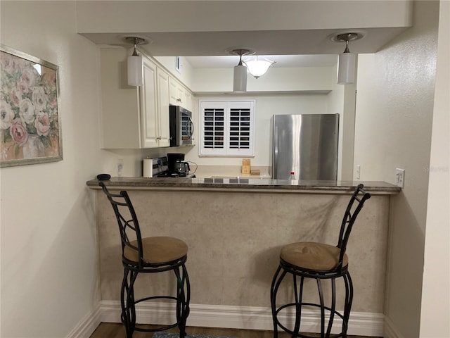 kitchen featuring pendant lighting, white cabinetry, wood-type flooring, and appliances with stainless steel finishes