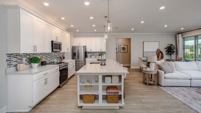 kitchen with appliances with stainless steel finishes, decorative light fixtures, white cabinetry, sink, and a center island with sink