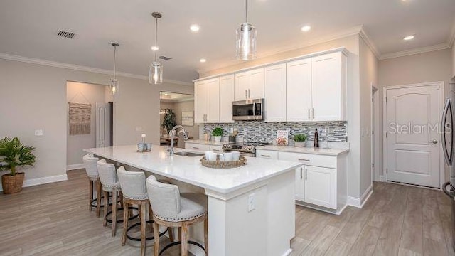 kitchen with pendant lighting, sink, appliances with stainless steel finishes, a kitchen island with sink, and white cabinets