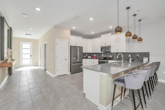 kitchen featuring stainless steel appliances, decorative light fixtures, kitchen peninsula, white cabinets, and backsplash