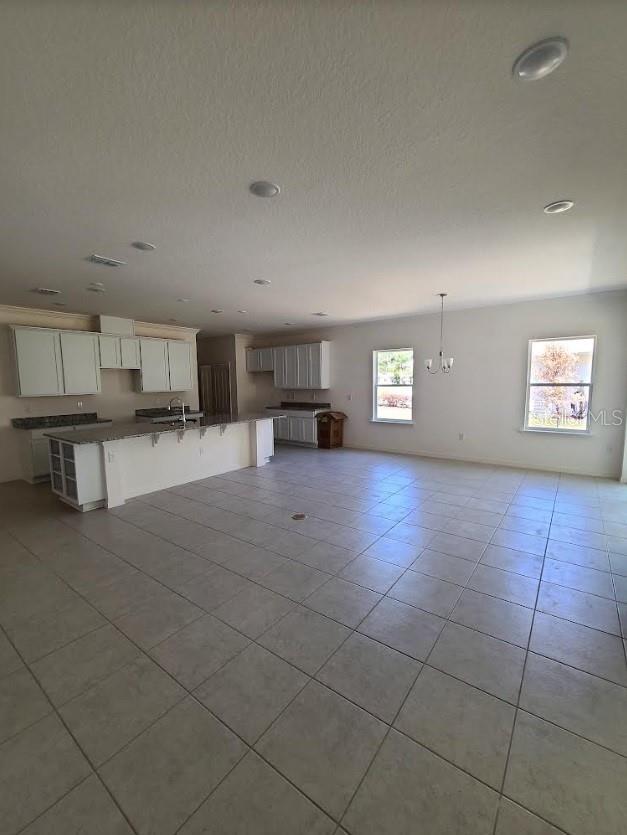 unfurnished living room featuring light tile patterned flooring, sink, and a notable chandelier