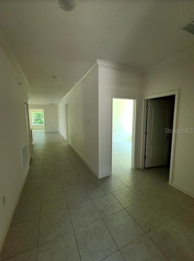 hallway featuring light tile patterned flooring, visible vents, and crown molding