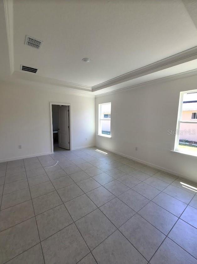 empty room featuring crown molding, light tile patterned floors, and a tray ceiling