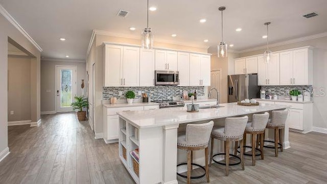 kitchen featuring appliances with stainless steel finishes, decorative light fixtures, a center island with sink, and white cabinets