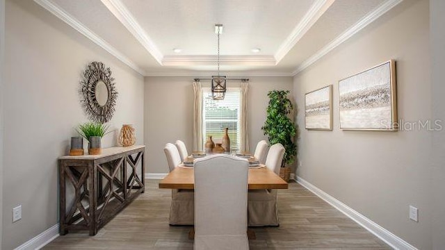 dining area with ornamental molding, wood finished floors, a raised ceiling, and baseboards