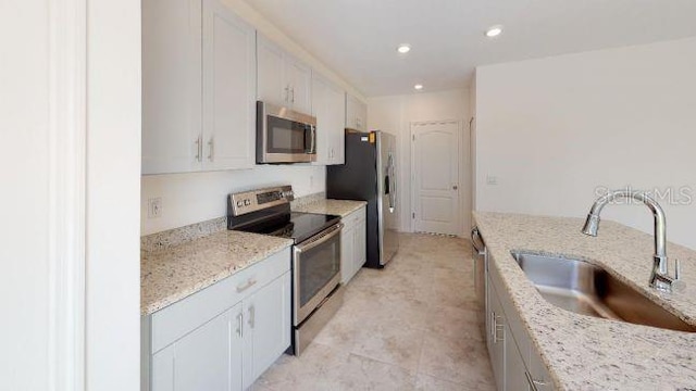 kitchen featuring white cabinetry, sink, stainless steel appliances, and light stone countertops