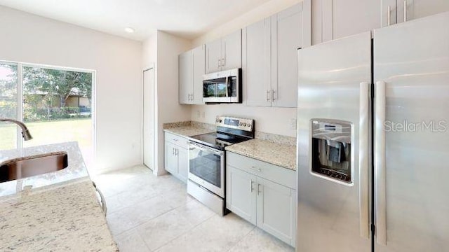 kitchen with sink, light stone counters, light tile patterned floors, appliances with stainless steel finishes, and white cabinets