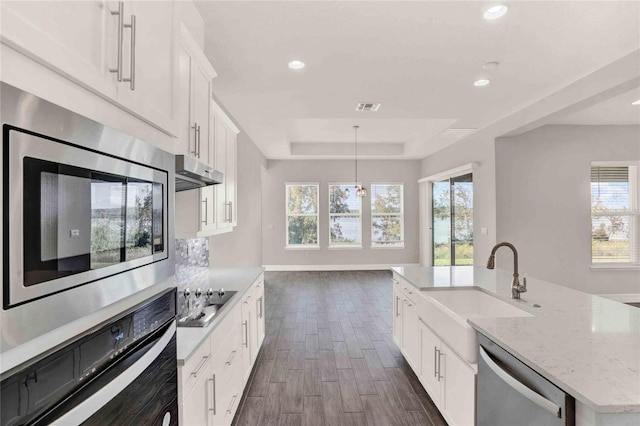 kitchen with a kitchen island with sink, dark wood-type flooring, decorative light fixtures, white cabinetry, and stainless steel appliances