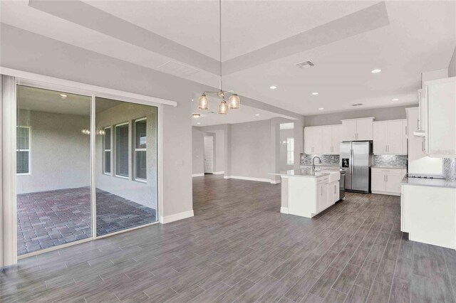 kitchen with stainless steel fridge, a kitchen island with sink, wood-type flooring, decorative light fixtures, and white cabinets