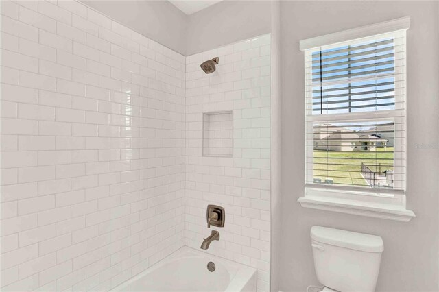 bathroom with a healthy amount of sunlight, toilet, and tiled shower / bath