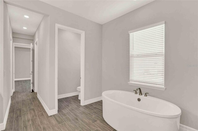 bathroom featuring a washtub, hardwood / wood-style floors, and toilet