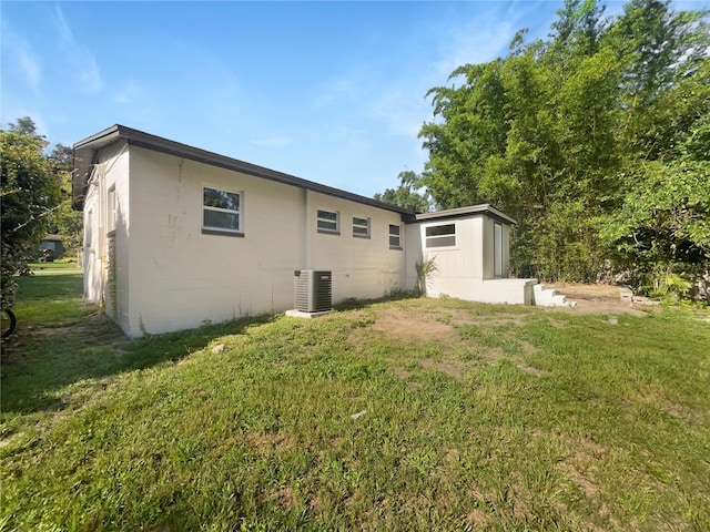 rear view of house with central AC unit and a yard