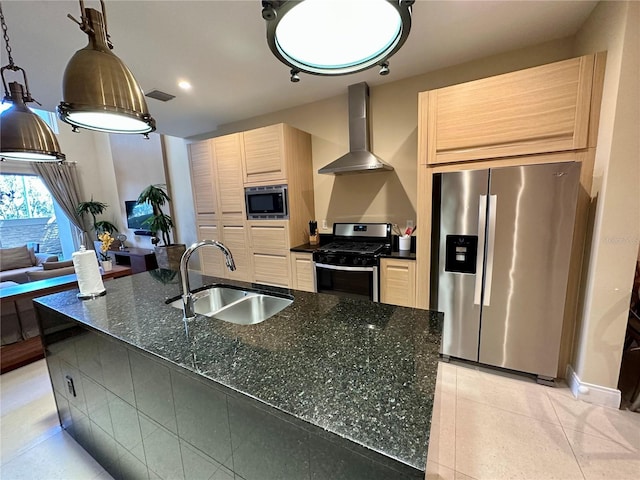 kitchen featuring light brown cabinets, sink, wall chimney range hood, dark stone countertops, and appliances with stainless steel finishes