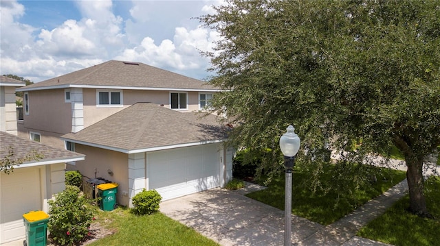 traditional home featuring a garage, concrete driveway, roof with shingles, and stucco siding