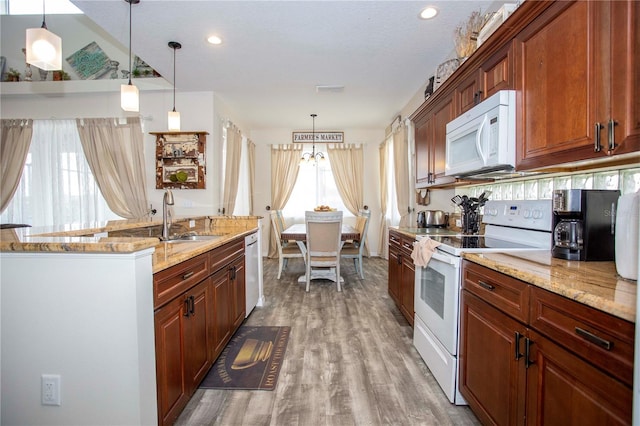 kitchen with white appliances, light stone counters, wood finished floors, decorative light fixtures, and a sink