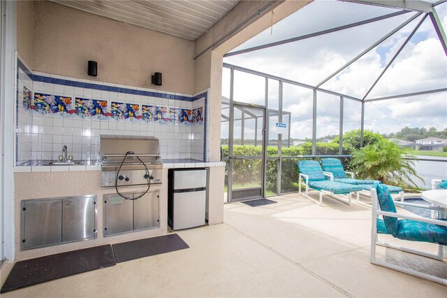 view of patio / terrace with exterior kitchen, a lanai, a sink, and grilling area