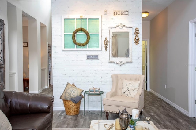 sitting room with brick wall, dark wood-type flooring, and baseboards