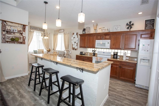 kitchen with white appliances, visible vents, dark wood-type flooring, hanging light fixtures, and a kitchen bar