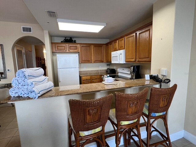 kitchen featuring a breakfast bar, white appliances, light tile patterned floors, and kitchen peninsula