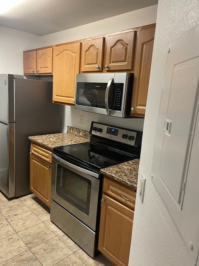 kitchen with dark stone counters, a textured ceiling, light tile flooring, and stainless steel appliances