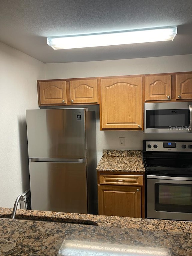 kitchen with appliances with stainless steel finishes and dark stone counters