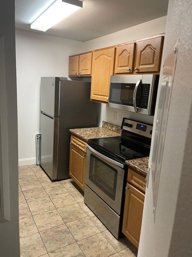 kitchen featuring dark stone counters, light tile floors, and appliances with stainless steel finishes