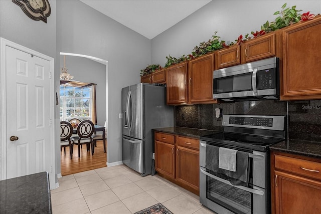 kitchen featuring appliances with stainless steel finishes, high vaulted ceiling, light tile floors, dark stone countertops, and tasteful backsplash