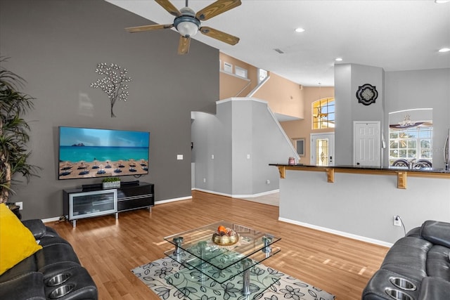 living room with a towering ceiling, ceiling fan, and light wood-type flooring