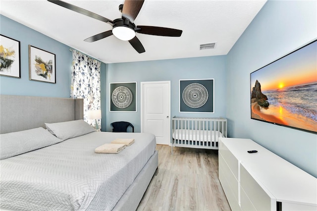 bedroom with a nursery area, ceiling fan, and light wood-type flooring