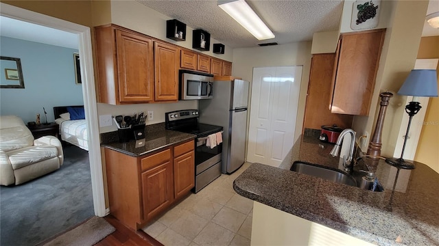 kitchen with light tile flooring, a textured ceiling, appliances with stainless steel finishes, dark stone countertops, and sink