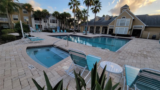 pool at dusk with a community hot tub and a patio