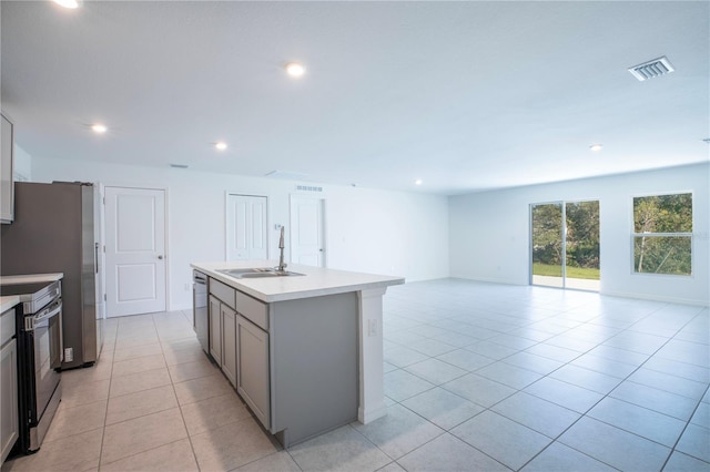 kitchen with a kitchen island with sink, sink, gray cabinets, light tile patterned floors, and stainless steel appliances