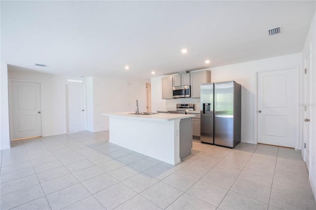 kitchen with gray cabinetry, sink, light tile patterned floors, an island with sink, and appliances with stainless steel finishes