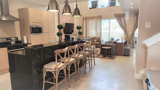 interior space featuring light tile floors, appliances with stainless steel finishes, wall chimney exhaust hood, and light brown cabinets