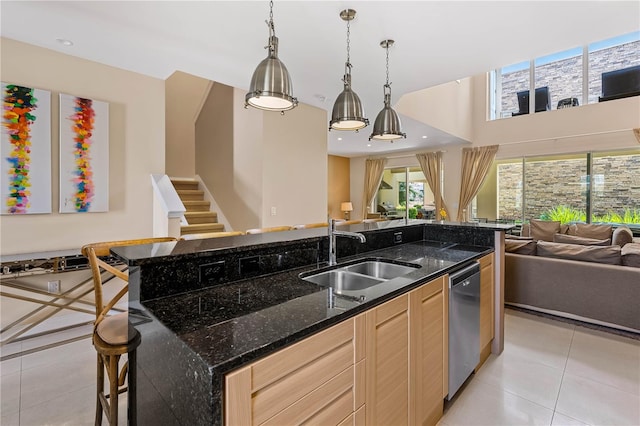 kitchen with light brown cabinetry, sink, dark stone counters, hanging light fixtures, and light tile flooring