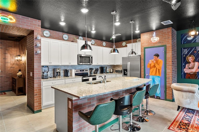 kitchen with appliances with stainless steel finishes, brick wall, backsplash, and a kitchen island with sink