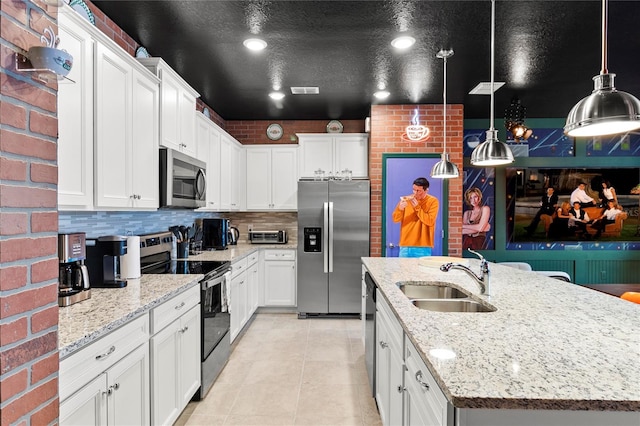 kitchen featuring an island with sink, pendant lighting, stainless steel appliances, brick wall, and sink