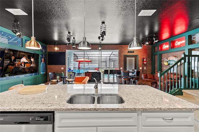 kitchen with white cabinets, light stone counters, stainless steel dishwasher, and sink