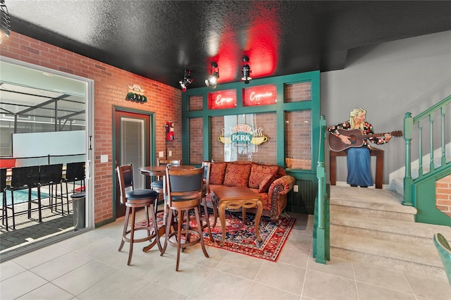 interior space featuring brick wall, indoor bar, a textured ceiling, and light tile floors